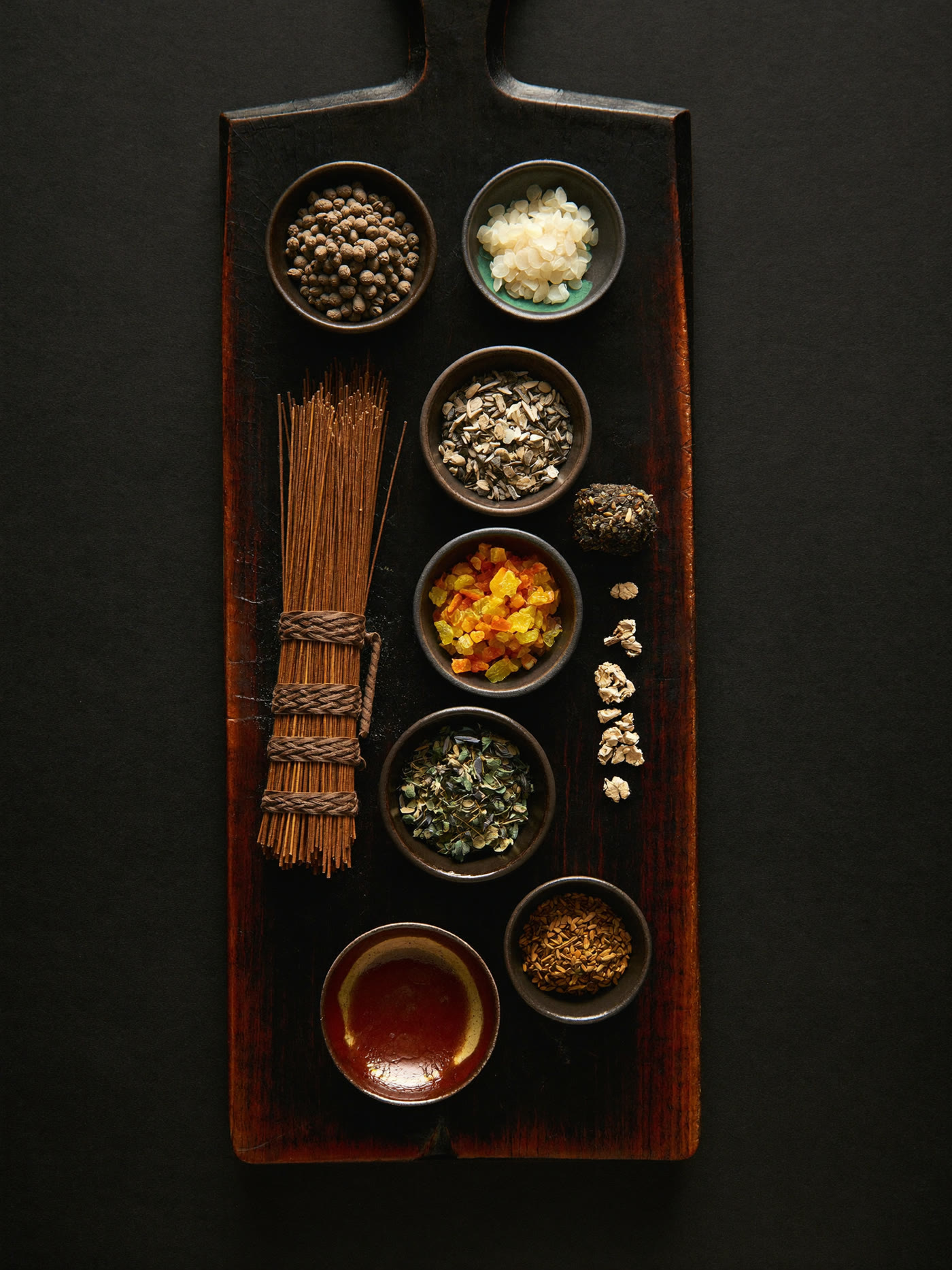 Raw incense ingredients in ceramic dishes on a dark board